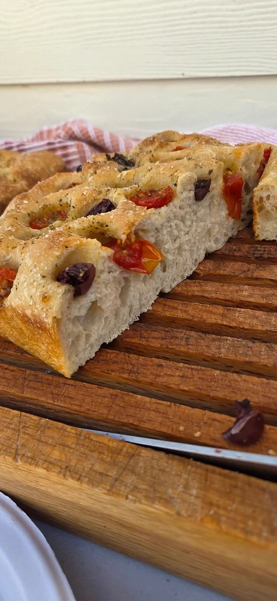 Sliced sourdough focaccia with tomatoes and olives showing its airy crumb on a wooden board
