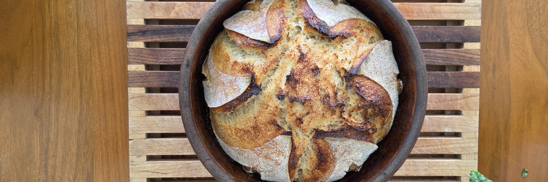 A scored sourdough loaf baked in a handmade earthenware baker